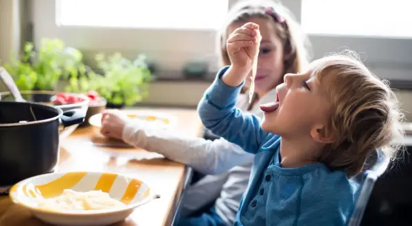 Große Schwester versucht, den kleinen Bruder zum Essen zu überreden, der nicht essen will.