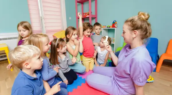 Lehrerin zeigt Kindern im Kindergarten eine Zahl. Alle Kinder sind aufmerksam, ein Zeichen für gelebte Inklusion.