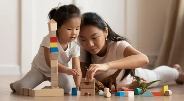 Mutter und Kind bauen mit Holzklötzen und Dinosauriern. Feinmotorik Kinder wird spielerisch gefördert.