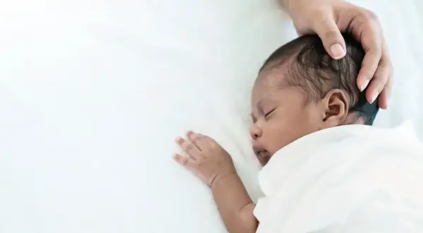 Ein süßes Baby schwitzt beim Schlafen am Kopf. Eine Hand streichelt sanft über das dunkle Haar.