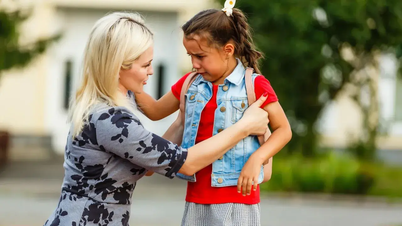 Mutter tröstet weinendes Kind mit Trennungsangst vor der Schule.