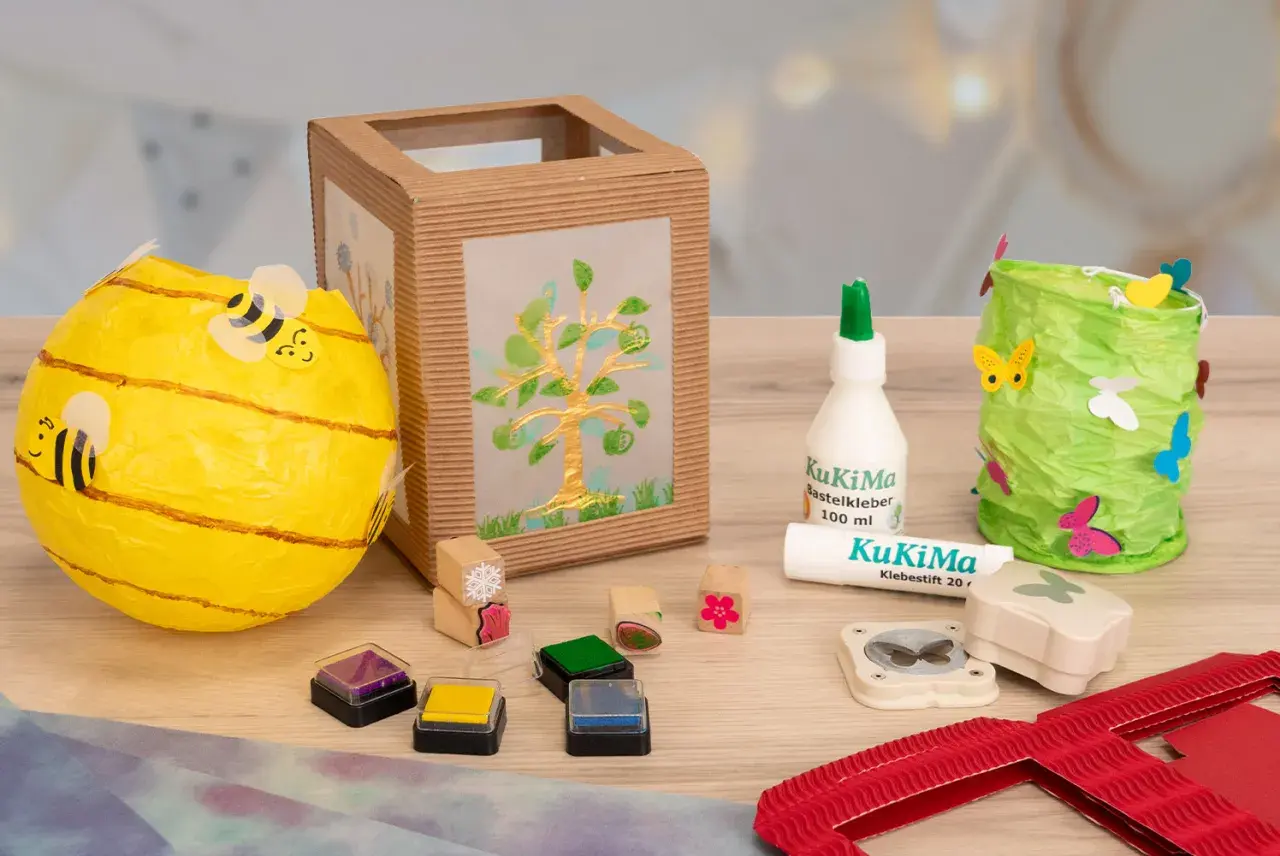 Bastelmaterialien für eine Laterne: Bienen-Laterne, Baum-Laterne, Kleber, Stempel & Schmetterlingsstanzer. Eine Vorlage zum Laterne basteln.