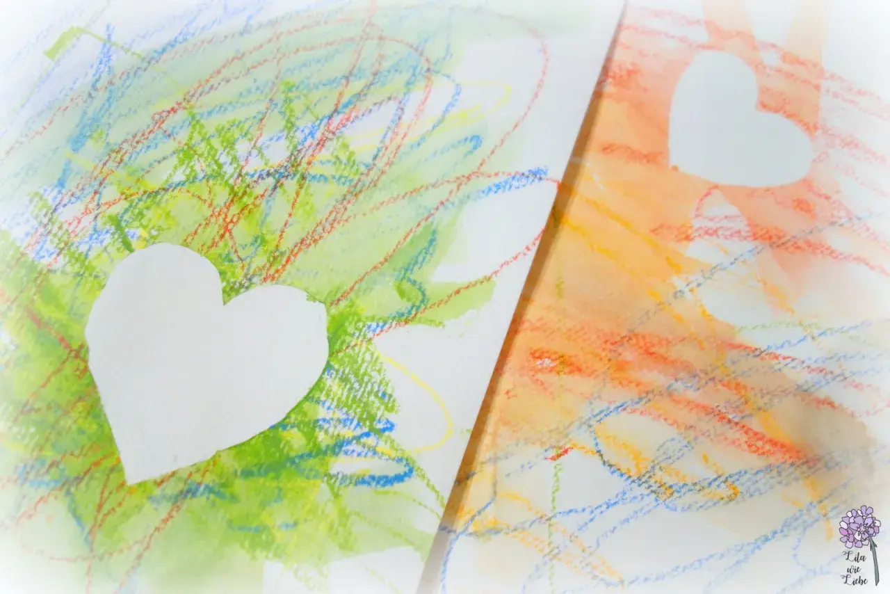 Bunte Kritzeleien, wie Kinder sie malen, mit weißen Herzen darauf. Ein Herz auf grünem, das andere auf orangem Hintergrund.
