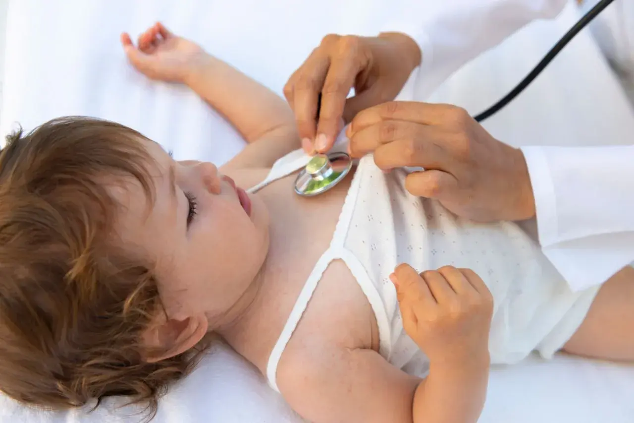 Arzt hört mit Stethoskop auf das Herz eines Babys. Eine U6 Untersuchung ist wichtig für die Gesundheit des Kindes.