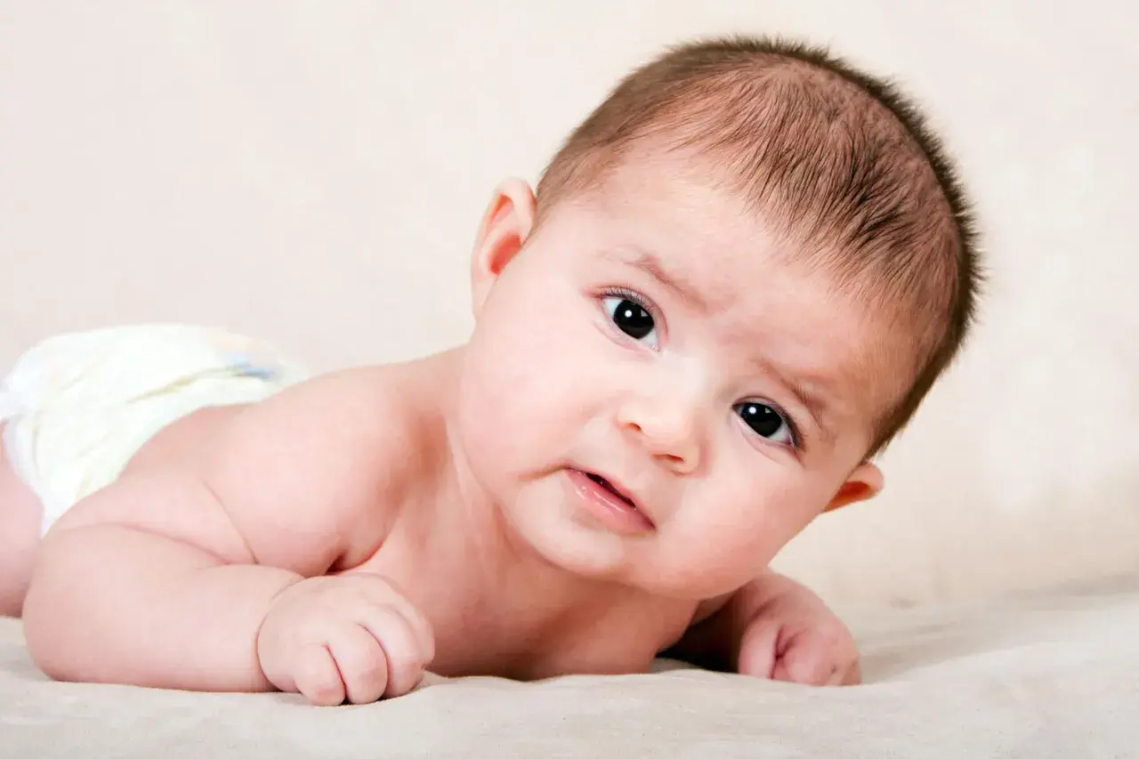 Ein süßes Baby, 4 Wochen alt, liegt auf dem Bauch und blickt neugierig in die Kamera.