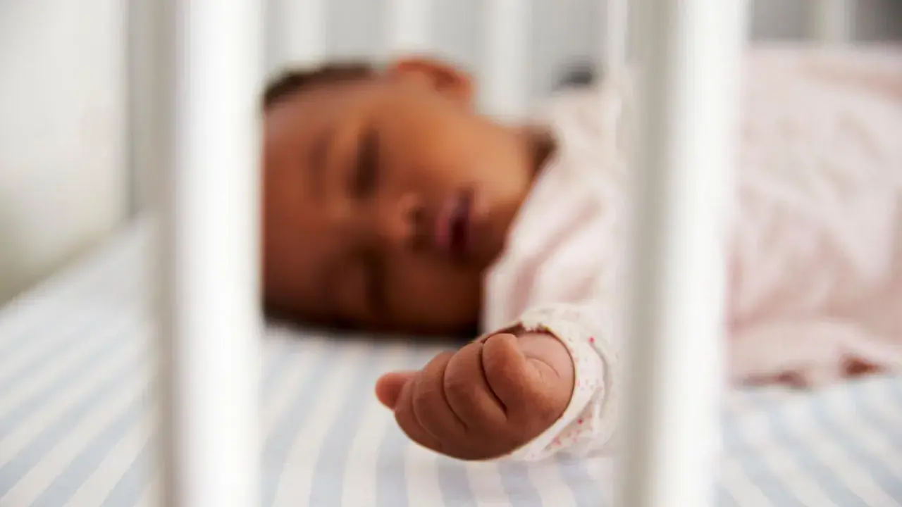 Ein Baby zuckt im Schlaf, seine kleine Hand liegt auf gestreifter Bettwäsche.