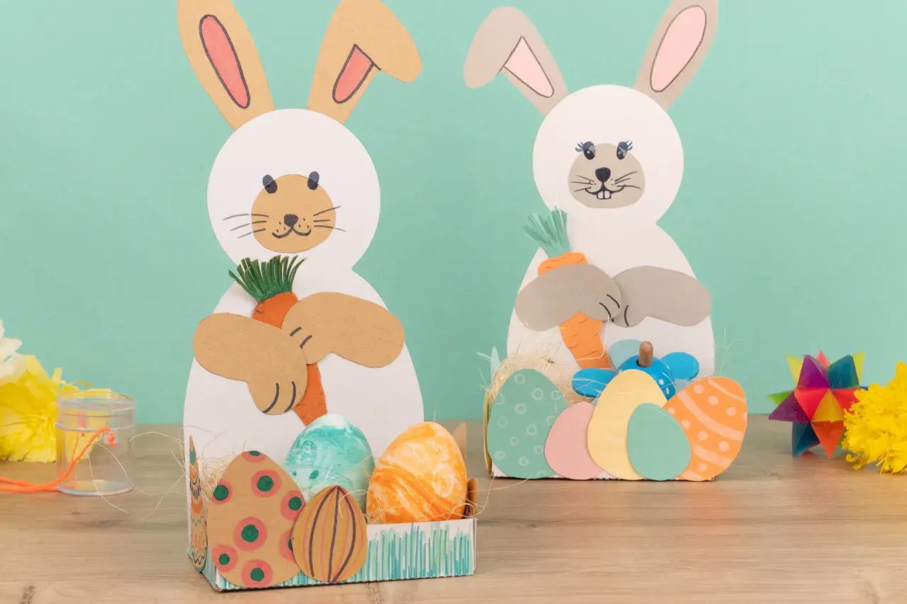 Zwei Bastelhasen mit Karotten und Ostereiern, eine schöne Idee für Ostern im Kindergarten.