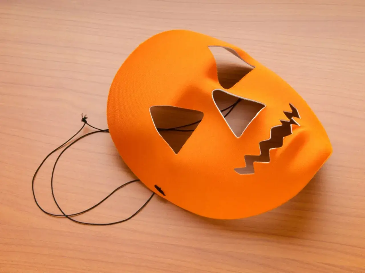Orange halloween maske basteln: Kürbisgesicht mit Zackenmund und dreieckigen Augen auf Holzhintergrund.