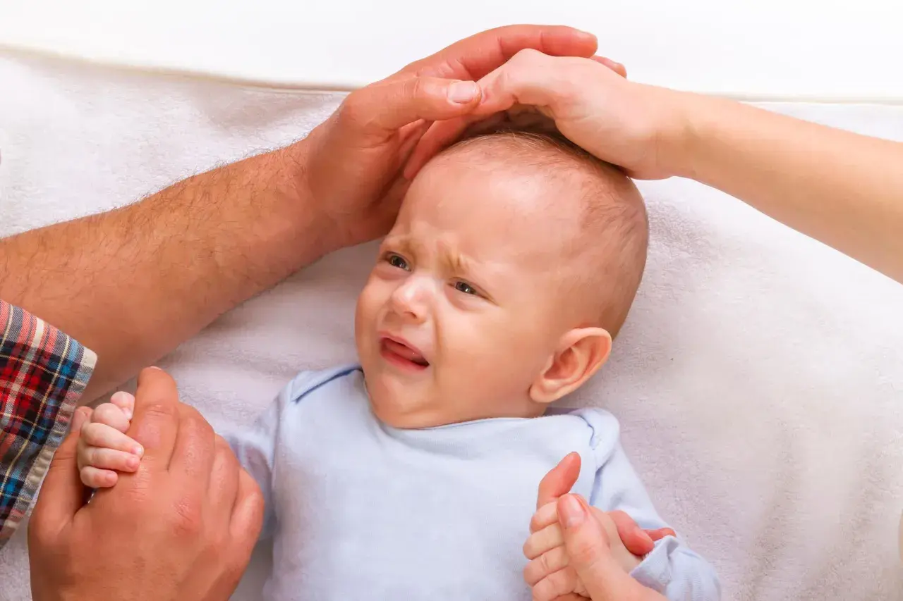 Ein weinendes Baby, 7 Wochen alt, wird von Elternhänden gehalten und getröstet.