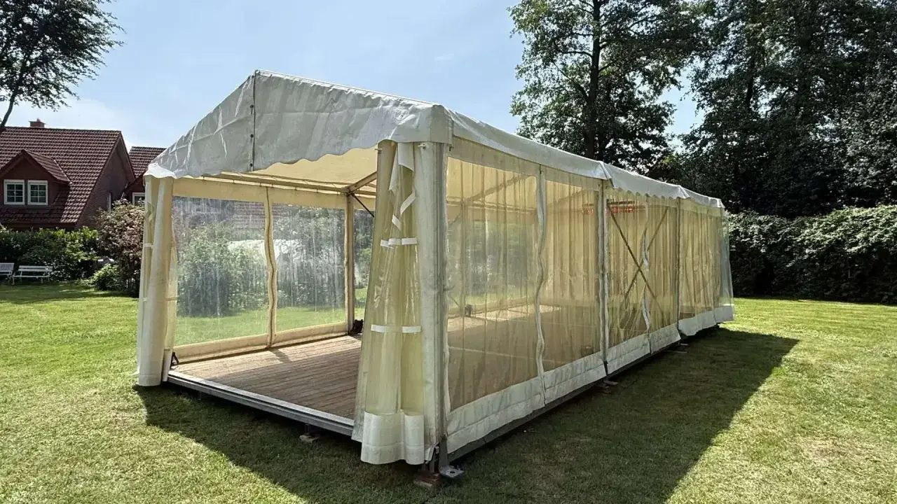 Ein Festzelt im Garten, bereit für eine Einschulungsfeier. Transparente Seitenwände lassen viel Licht herein.