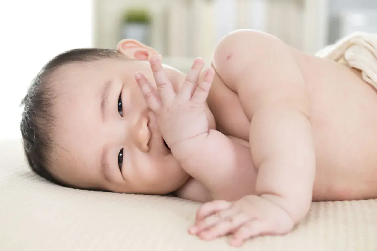 Ein süßer **baby 11 wochen** alt liegt auf der Seite und bedeckt seinen Mund mit der Hand.