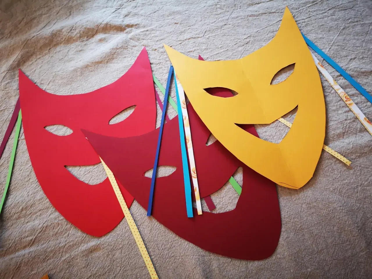 Bunte Karneval Maske Vorlagen liegen auf Stoff. Rot, dunkelrot und gelb. Bänder in verschiedenen Farben stecken an den Masken.