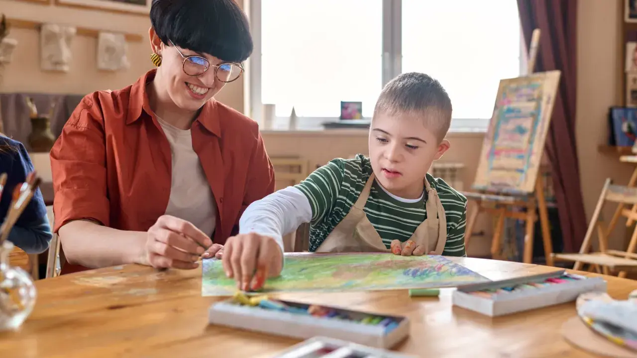 Lehrerin unterstützt Jungen mit Down-Syndrom beim Malen. Erste Eindrücke für die Eingangsdiagnostik Grundschule.