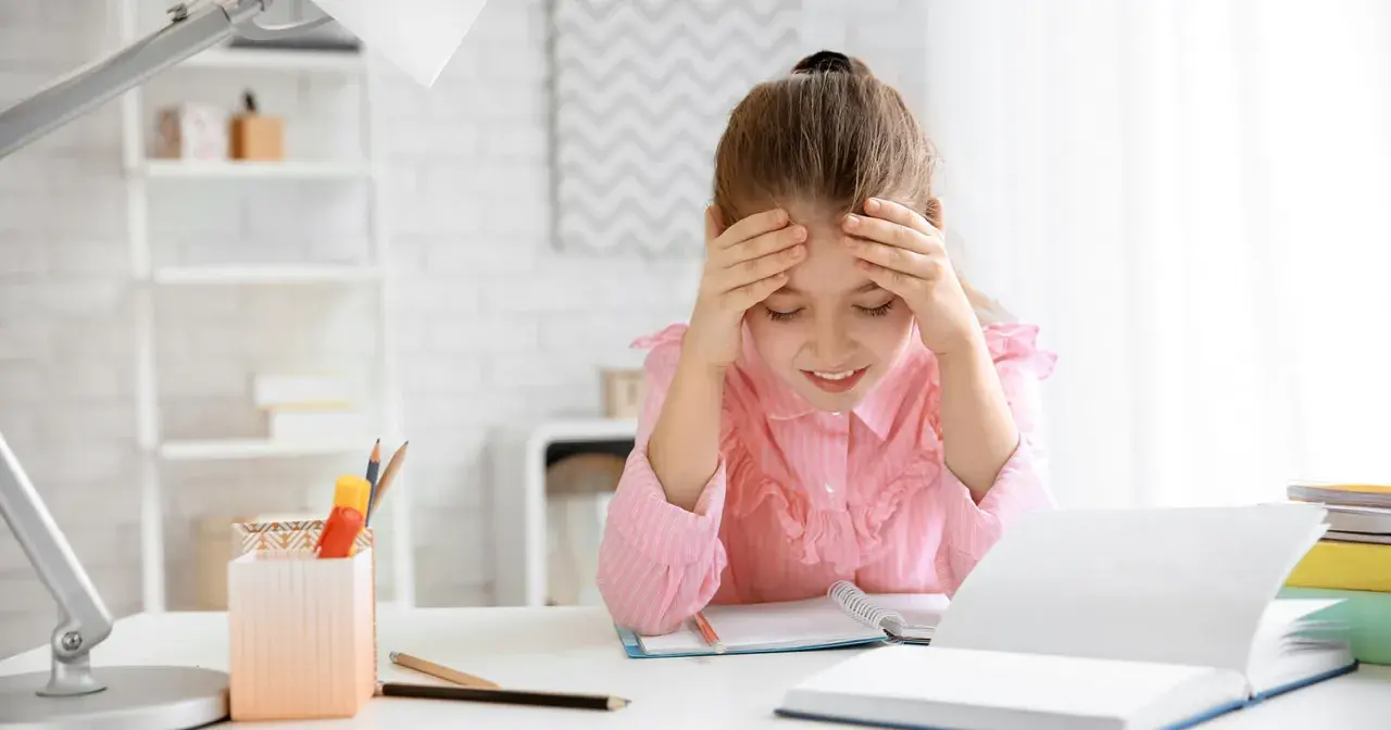 Ein Mädchen mit Händen an der Stirn, das über seinen Büchern sitzt. Die **Stress Kinder** sind deutlich zu sehen.
