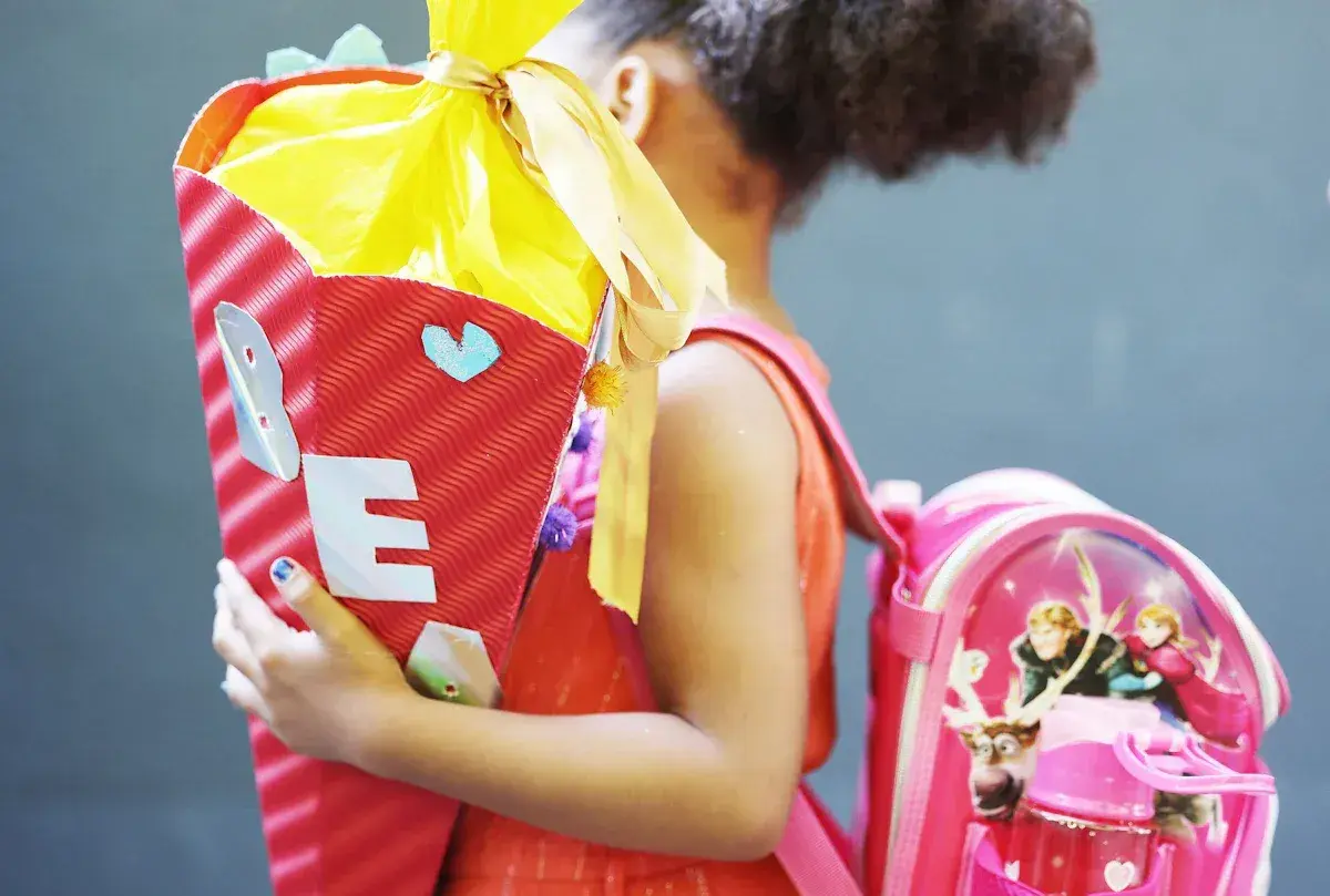 Ein Mädchen feiert die Einschulung mit einer bunten Zuckertüte und einem Rucksack mit Frozen-Motiv.