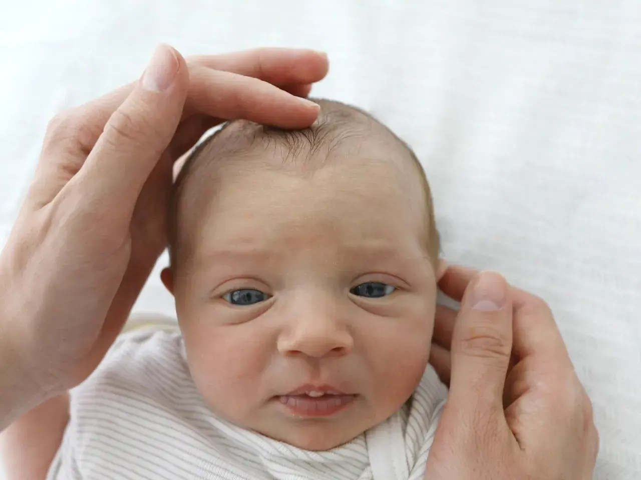 Sanft berühren die Hände eines Elternteils das Köpfchen eines Babys. Die Fontanelle ist leicht eingefallen, ein Zeichen für mögliche Dehydrierung.