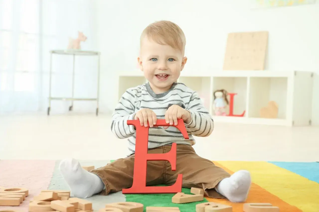 Ein lächelnder Junge hält den roten Buchstaben "E". Vielleicht ein zukünftiger Elias oder Emil, einer der vielen Jungennamen mit E.