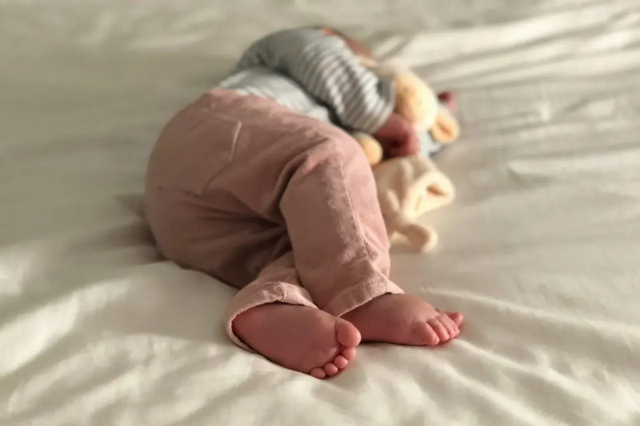 Ein Baby schläft auf einer weißen Decke, die Füße nach vorne gestreckt. Es ist ein Zeichen für einen Wachstumsschub, wenn Babys so tief und fest schlafen.