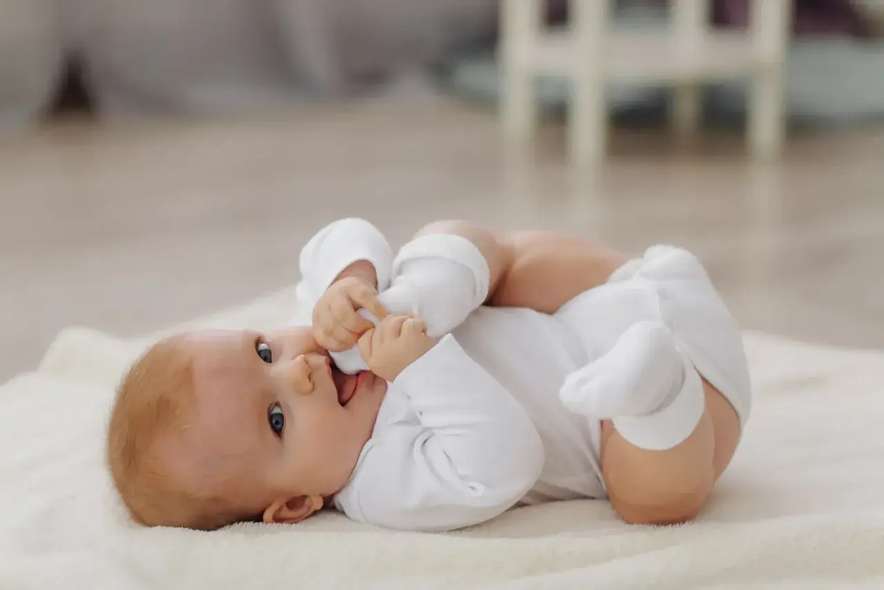 Ein süßes Baby, 8 Wochen alt, liegt auf einer weichen Decke und spielt mit seinen Füßen.