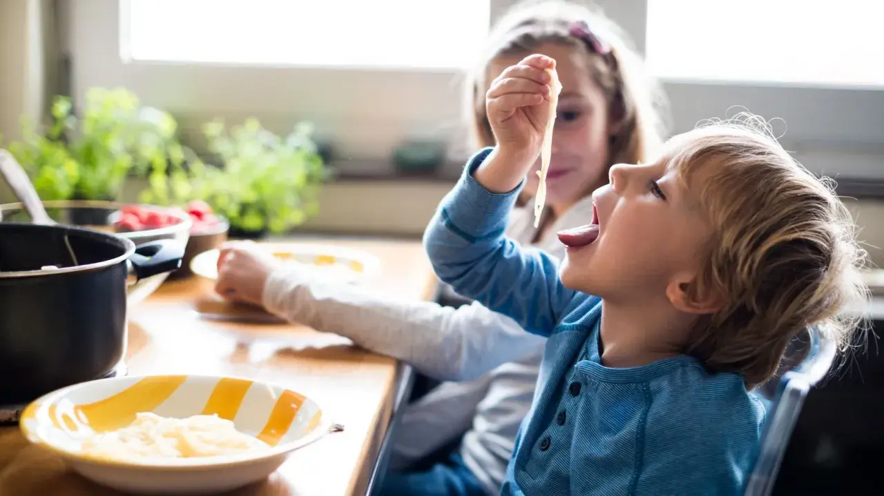 Große Schwester versucht, den kleinen Bruder zum Essen zu überreden, der nicht essen will.