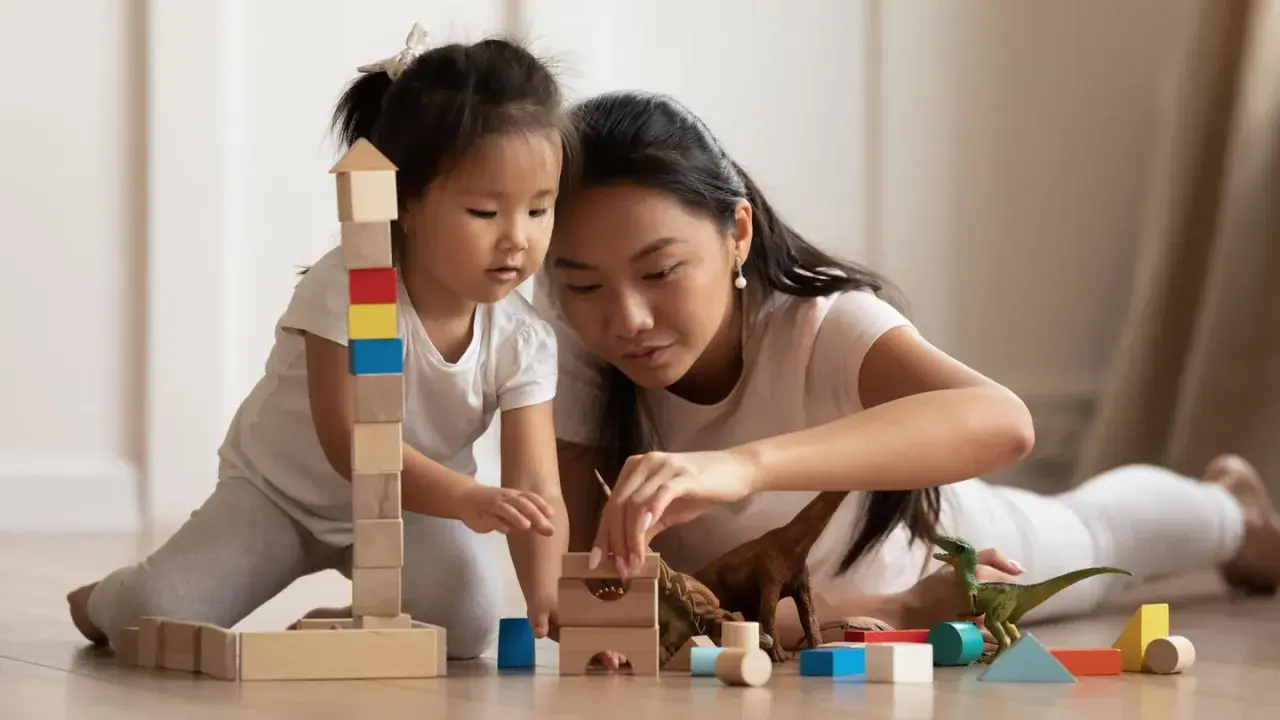 Mutter und Kind bauen mit Holzklötzen und Dinosauriern. Feinmotorik Kinder wird spielerisch gefördert.