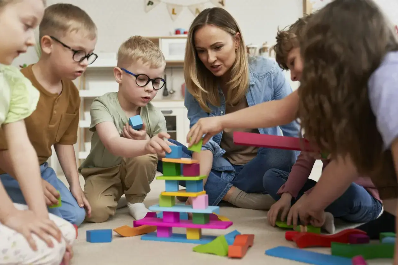 Kinder und Erzieherin bauen gemeinsam einen Turm. Dabei üben sie spielerisch soziale Kompetenzen wie Teamwork und Kommunikation.