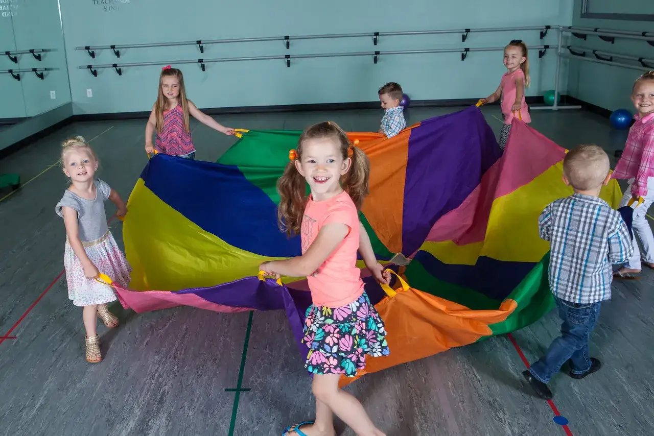 Kinder haben Spaß bei Bewegungsspielen im Kindergarten und halten einen bunten Fallschirm.