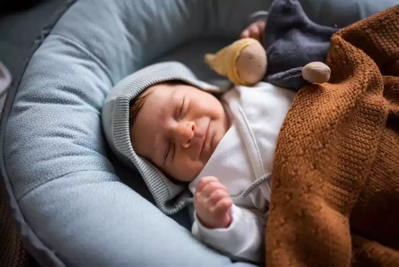 Ein friedlich schlafendes Baby, nur 2 Wochen alt, in einer kuscheligen Nestchen. Ein Sternchen-Stofftier wacht über den süßen Traum.