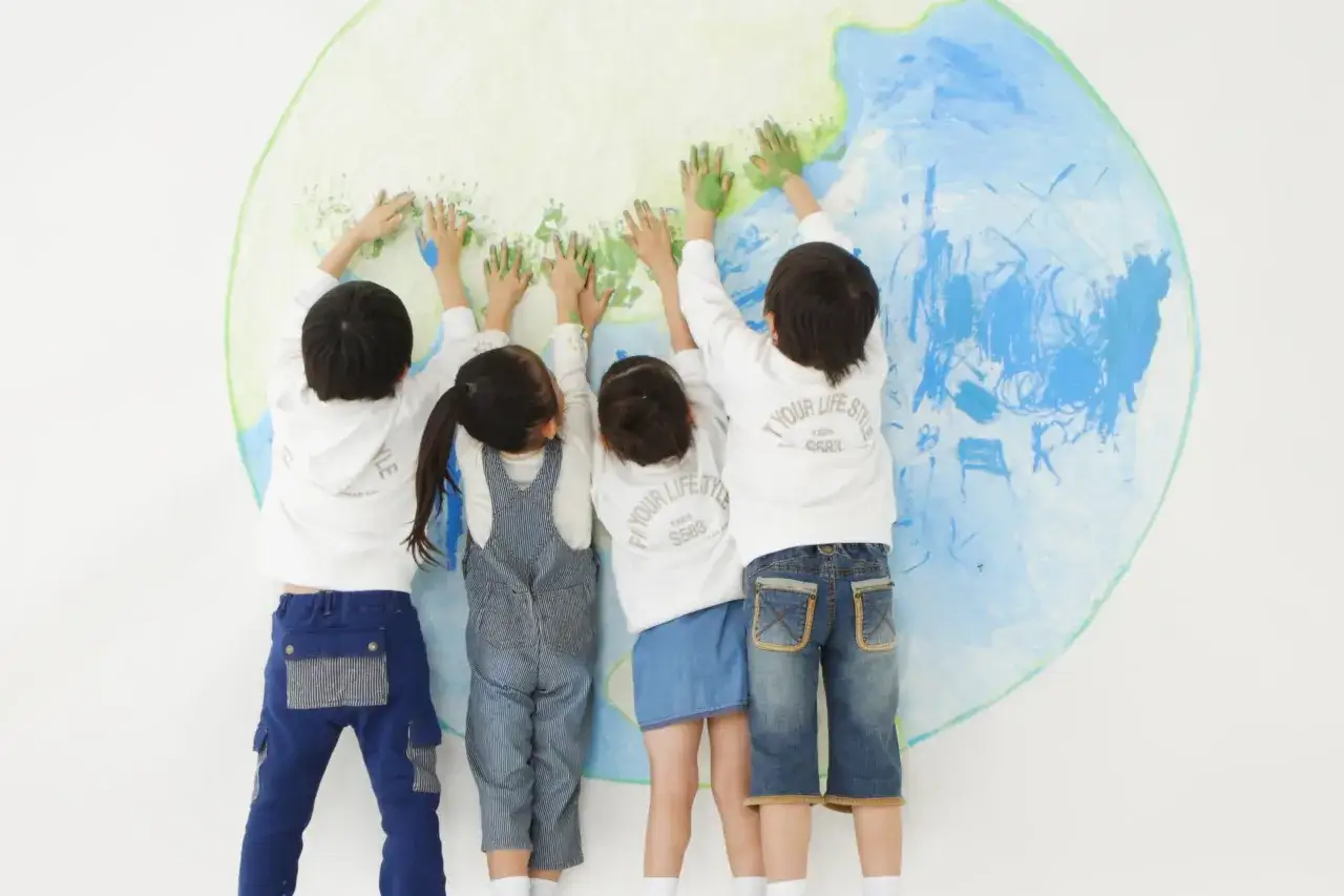 Kinder bemalen einen Globus mit ihren Händen. Dies ist ein Beispiel für interkulturelle Erziehung im Kindergarten, bei dem Kinder lernen, die Welt gemeinsam zu gestalten.