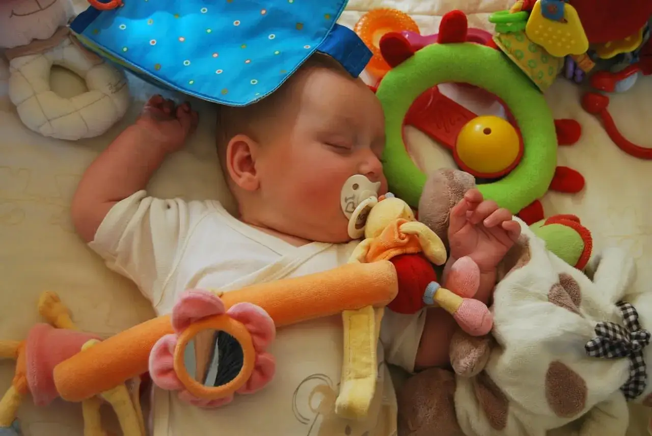 Schlafendes Baby mit Schnuller und Spielzeug. Ab wann Schnuller Baby? Diese Frage stellen sich viele Eltern.