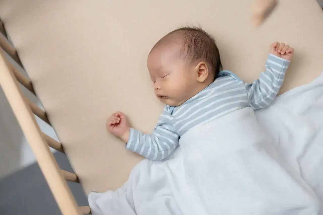 Ein kleines Baby mit blauen Streifen schläft friedlich in seinem Bettchen. Es zuckt im Schlaf, die kleinen Fäuste geballt.