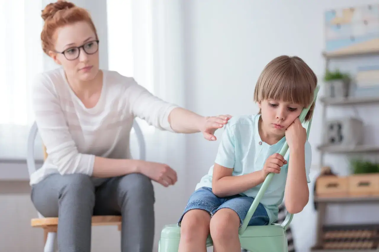 Ein Junge mit traurigem Blick, der die Hand ans Kinn legt. Eine Frau legt ihm tr&ouml;stend die Hand auf die Schulter. M&ouml;gliche selektiver mutismus symptome.