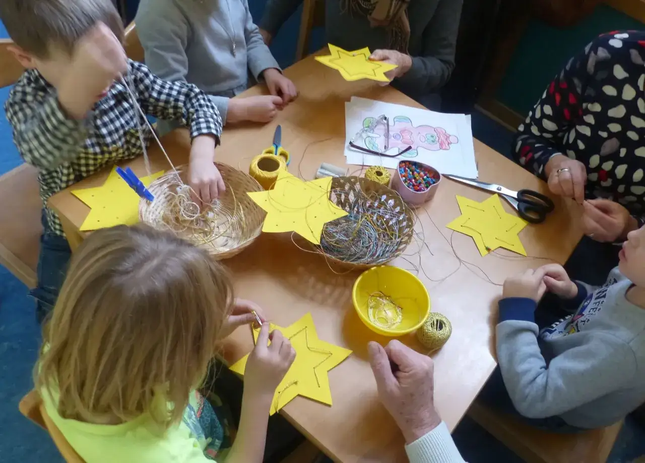Kinder basteln Sterne mit Oma und Opa. Bunte F&auml;den und Perlen liegen bereit.