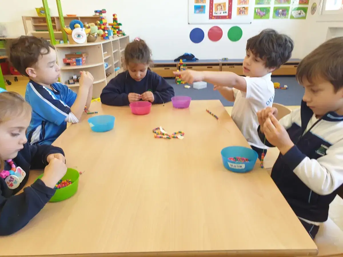 Kindergartenkinder basteln Freundschaftsbänder. Sie fädeln bunte Perlen auf Schnüre und zeigen ihre Werke.