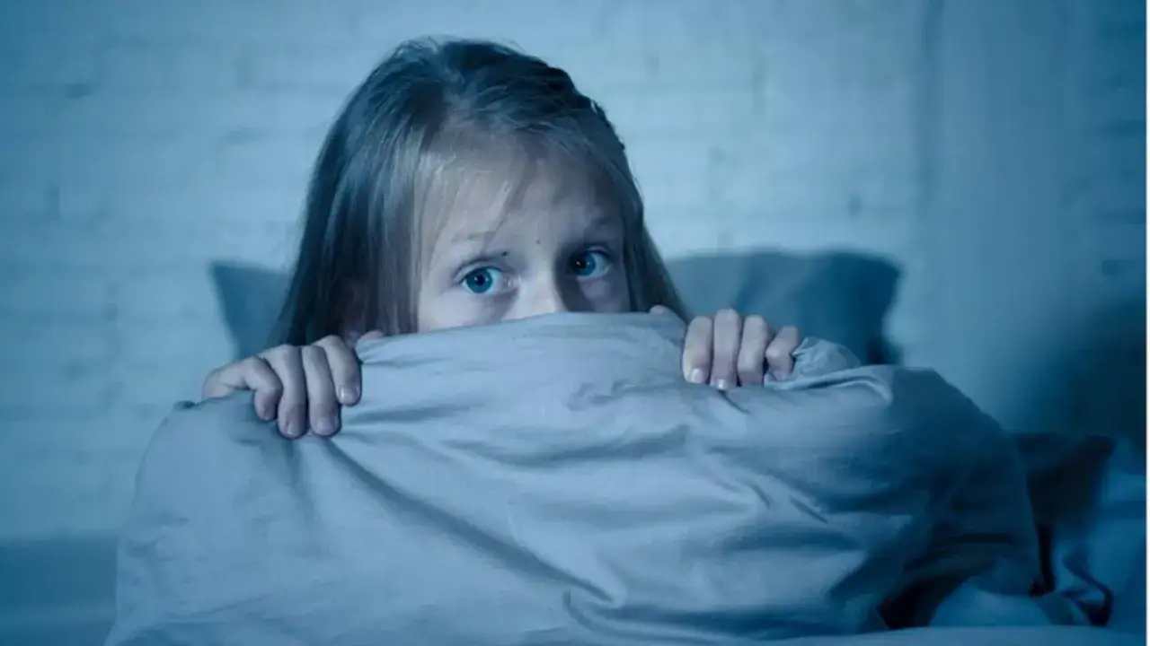 Ein Kind hat Angst vor Monstern und versteckt sich unter der Decke. Die blauen Augen blicken ängstlich hervor.