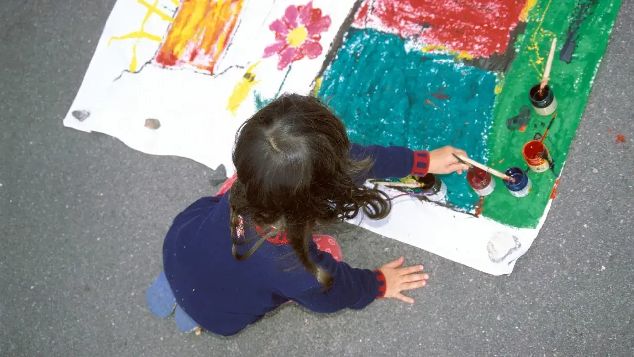 Ein Kind malt auf einem gro&szlig;en Blatt Papier. Die bunten Farben und die Art der Zeichnung k&ouml;nnten auf die Verarbeitung von kinderzeichnungen trauma hindeuten.