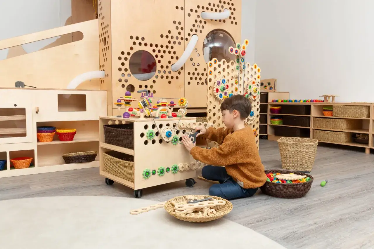 Ein Junge spielt konzentriert mit einem Montessori-Spielturm, der seine motorischen F&auml;higkeiten f&ouml;rdert.