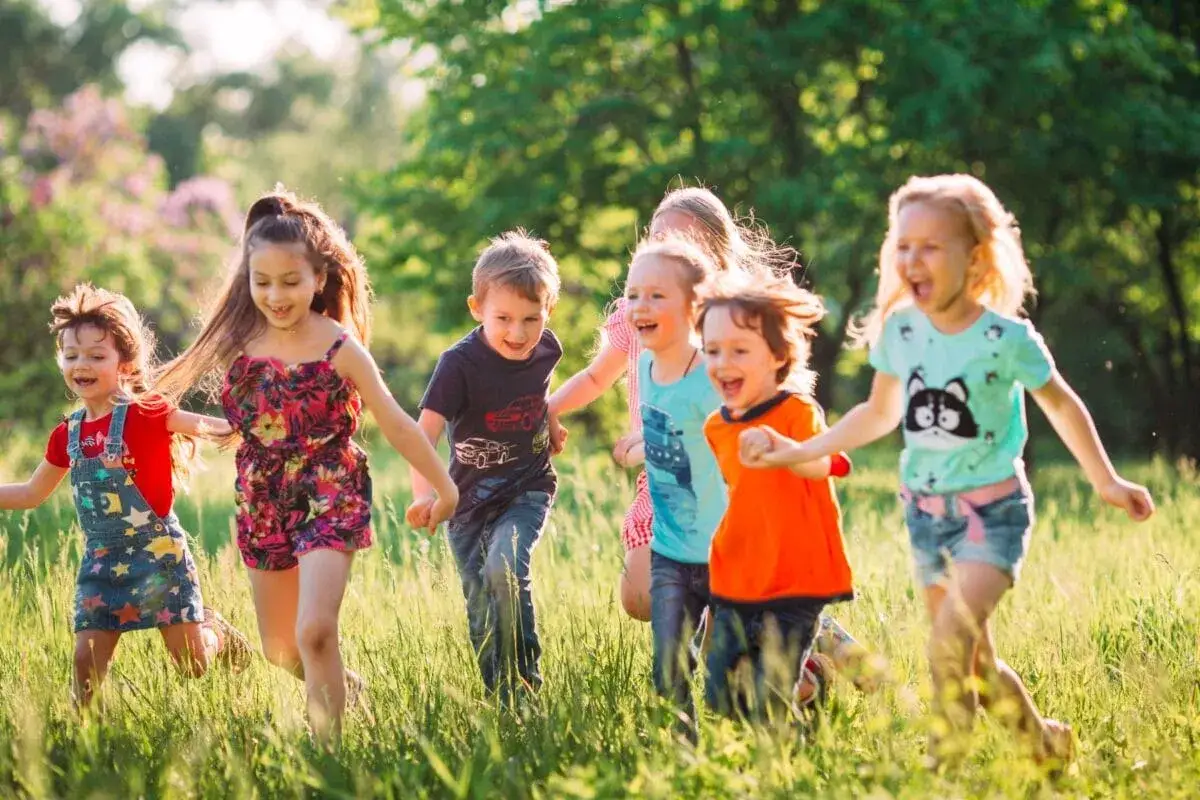 Gl&uuml;ckliche Kinder rennen lachend im Gras. Ein Kind findet keine Freunde, aber hier sind alle zusammen.