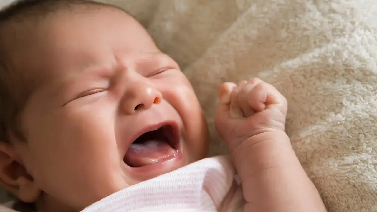 Ein baby schreit im schlaf, die Augen geschlossen, der Mund weit geöffnet. Ein kleiner Arm ist zur Faust geballt.