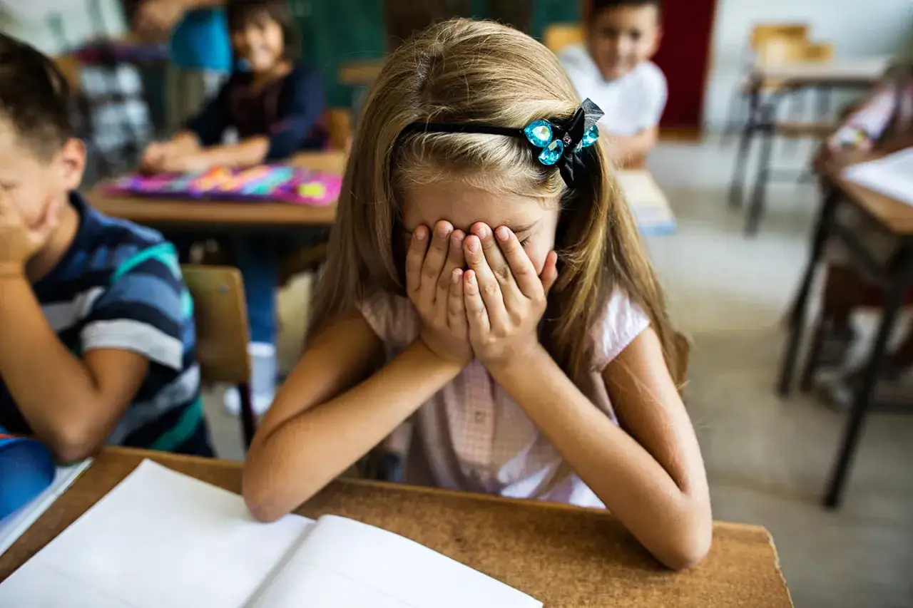 Ein M&auml;dchen versteckt ihr Gesicht in den H&auml;nden, offensichtlich &uuml;berfordert. Andere Kinder im Hintergrund scheinen unbeschwert, was den Stress des M&auml;dchens unterstreicht.