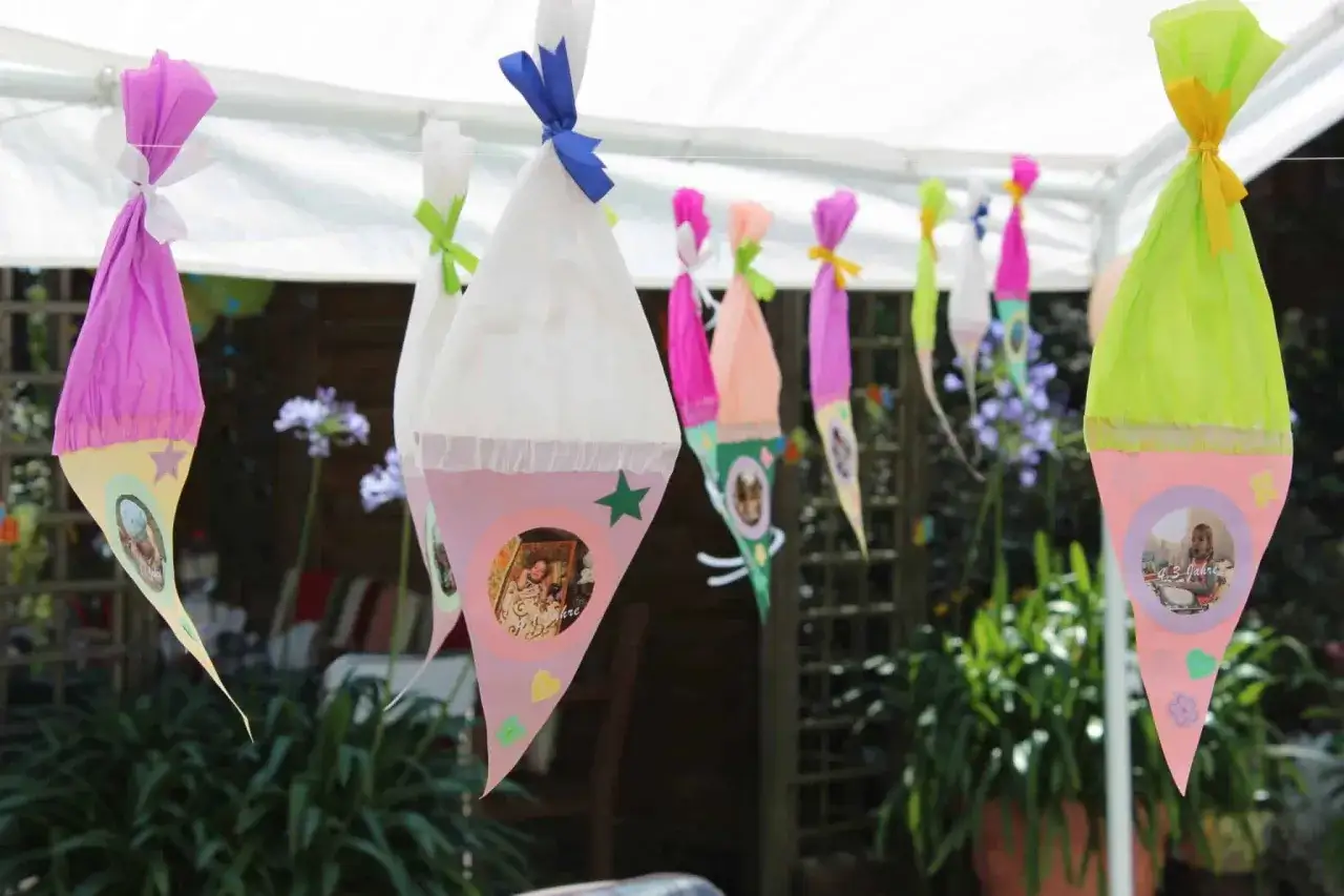 Bunte Schultüten-Girlanden im Garten für eine Einschulungsfeier. Jede Tüte ist mit Fotos von Kindern und kleinen Sternen verziert.