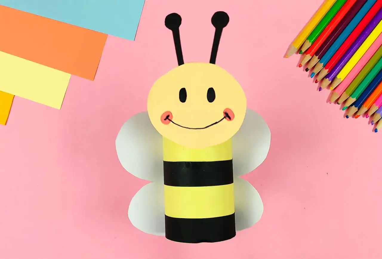 Bastelidee: Eine fröhliche Biene aus Papierrollen, mit bunten Stiften und Papier im Hintergrund.