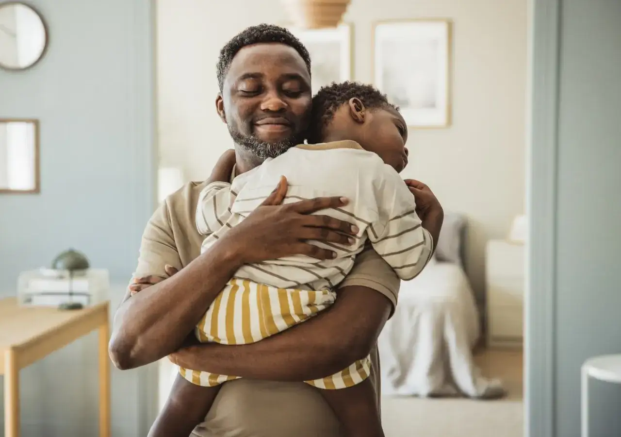 Ein Vater hält sein schlafendes Kind fest. Liebevolle Umarmungen sind ein Weg, wie bekommt mein Kind mehr Selbstbewusstsein.