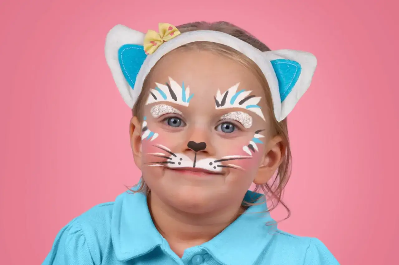 Ein Kind mit Katzen-Schminke und Ohren. Das Gesicht ist mit weißen, blauen und schwarzen Streifen bemalt, die Schnurrhaare und Wangen sind rosa.
