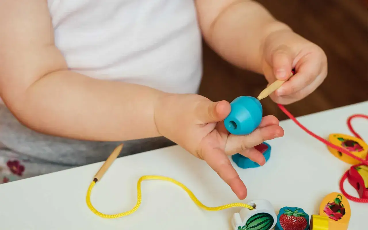 Kleine Hände üben feinmotorik kinder beim Auffädeln bunter Holzperlen.
