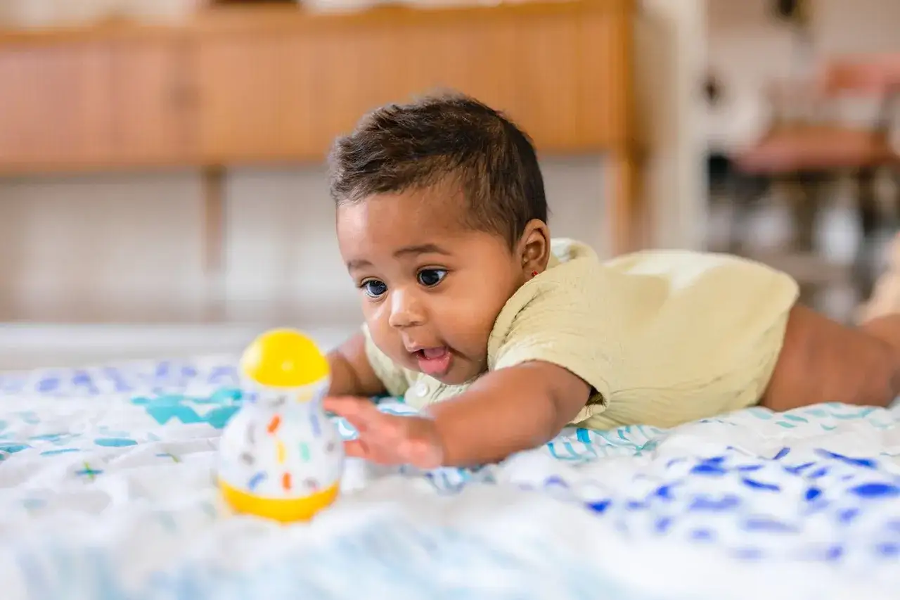 Ein baby 19 wochen alt liegt auf dem Bauch und streckt die Hand nach einem bunten Spielzeug aus.