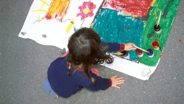 Ein Kind malt auf einem großen Blatt Papier. Die bunten Farben und die Art der Zeichnung könnten auf die Verarbeitung von kinderzeichnungen trauma hindeuten.