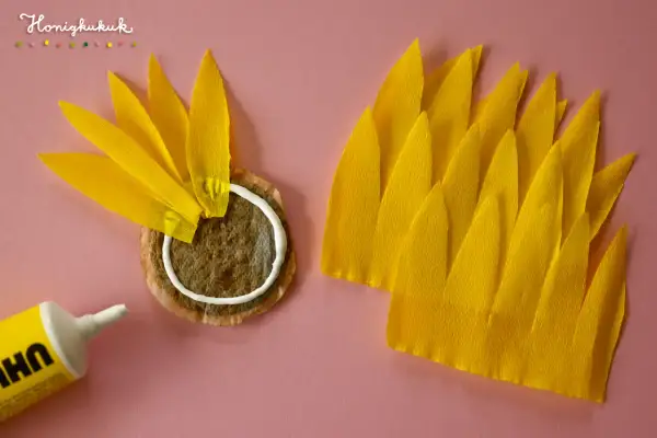 Sonnenblume basteln Krippe: Gelbe Blütenblätter aus Krepppapier werden auf einen Teebeutel geklebt.