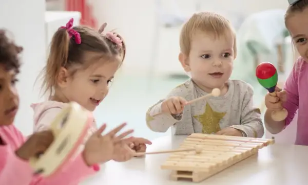 Kinder haben Spaß mit Musik im Kindergarten. Sie spielen Xylophon, Tamburin und Maracas.