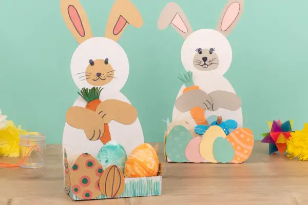 Zwei Bastelhasen mit Karotten und Ostereiern, eine schöne Idee für Ostern im Kindergarten.